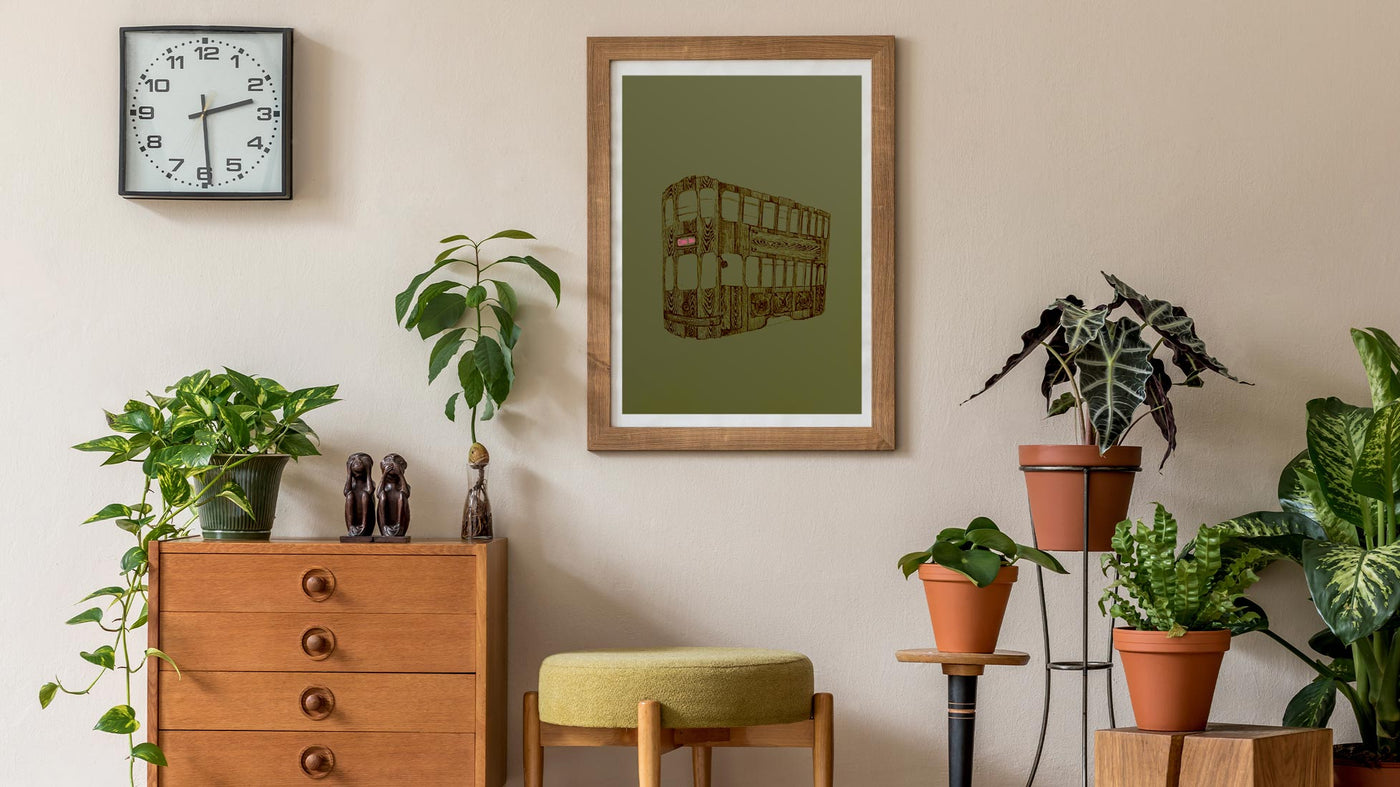 Framed olive green art print displayed above green house plants.