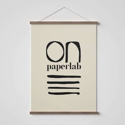 Wooden poster hanger with beige poster of On Paper Lab logo.